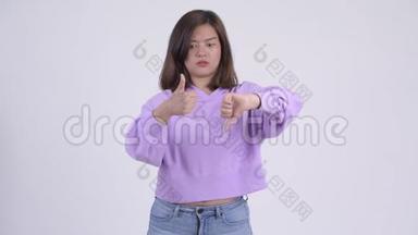 年轻迷茫的亚洲女人在竖起大拇指和大拇指之间做出选择
